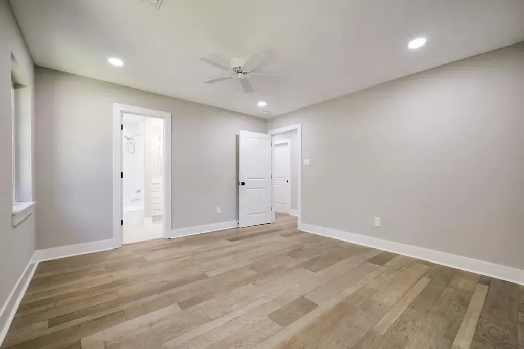 Empty beige room with hardwood floors, white trim, recessed lights, and two open doorways