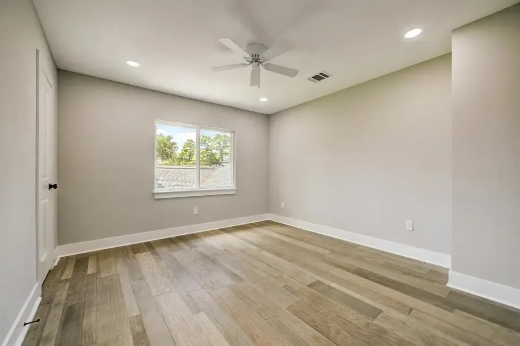 Empty beige bedroom with wood floors, a window, and a ceiling fan.