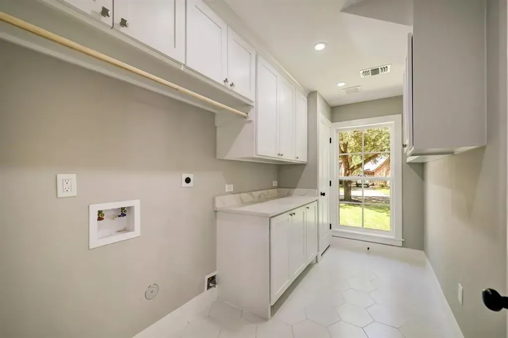 Bright narrow laundry room with white cabinets, countertop, and a door to a sunlit yard.