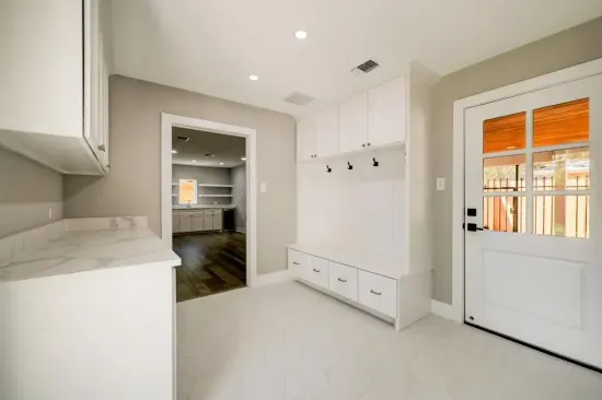 Bright white entry hall with built-in bench, coat hooks, and a door with orange curtains.