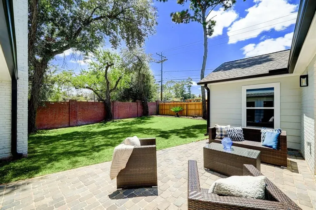 Sunny backyard patio with wicker seating, green lawn, trees, and a white house exterior