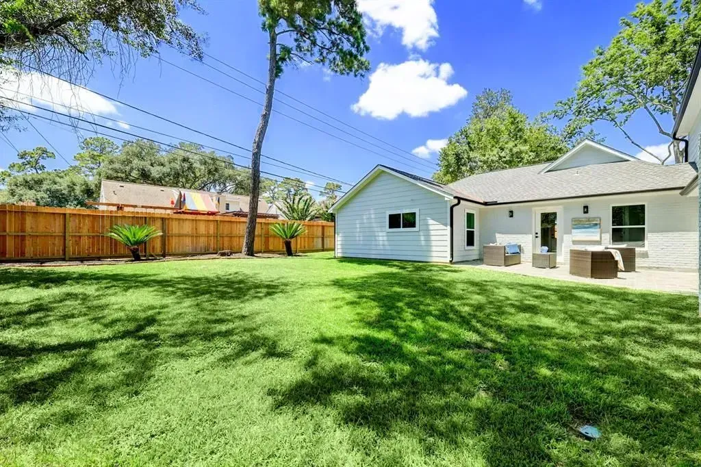 Sunny backyard with green lawn, wooden fence, small shed, and a white patio house under a blue sky