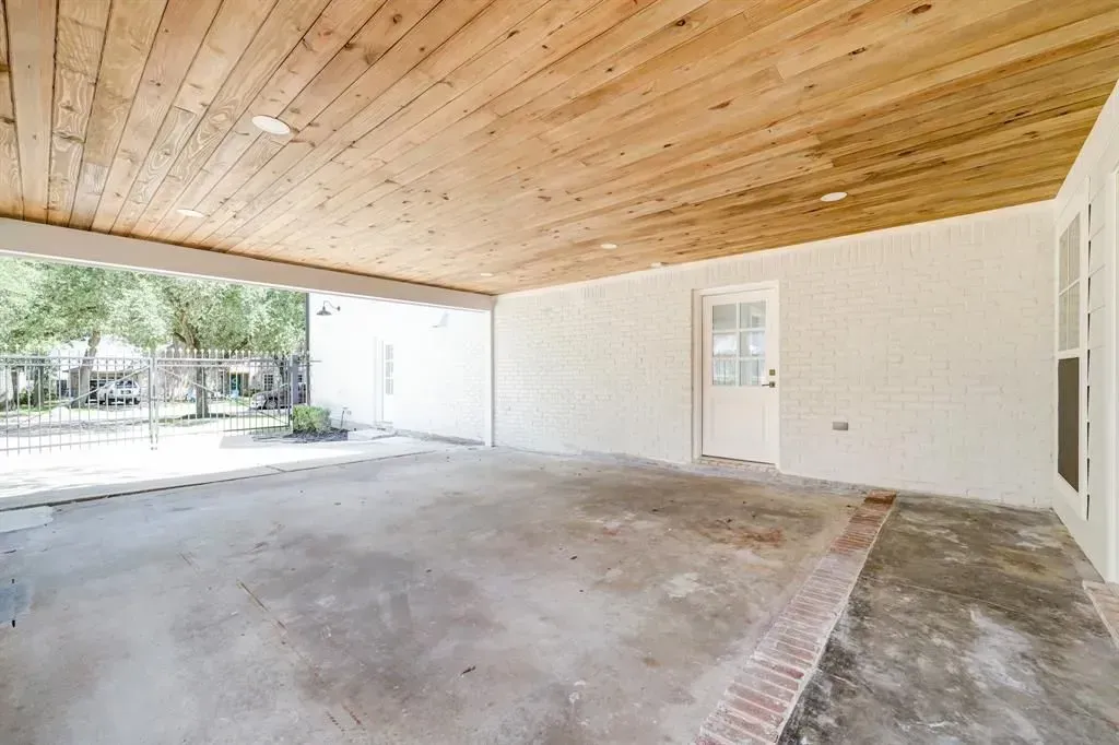 Covered patio with wooden ceiling, concrete floor, and white walls opening to a yard.