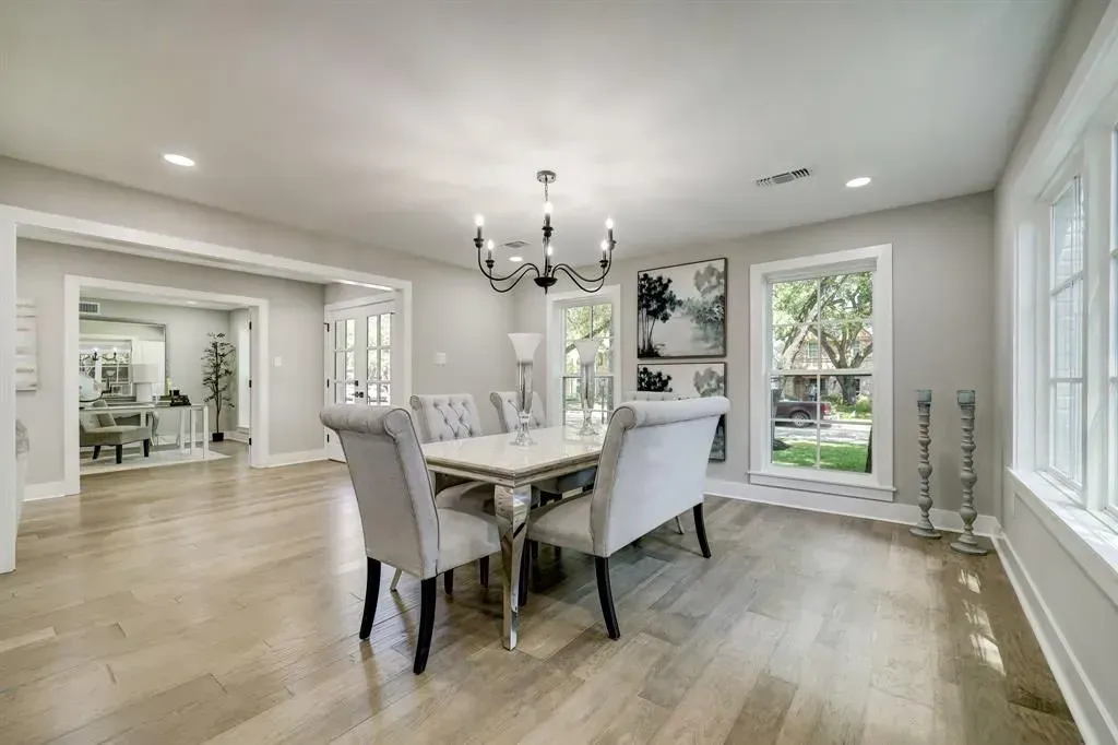 Bright dining room with a table, upholstered chairs, chandelier, and large windows overlooking trees.