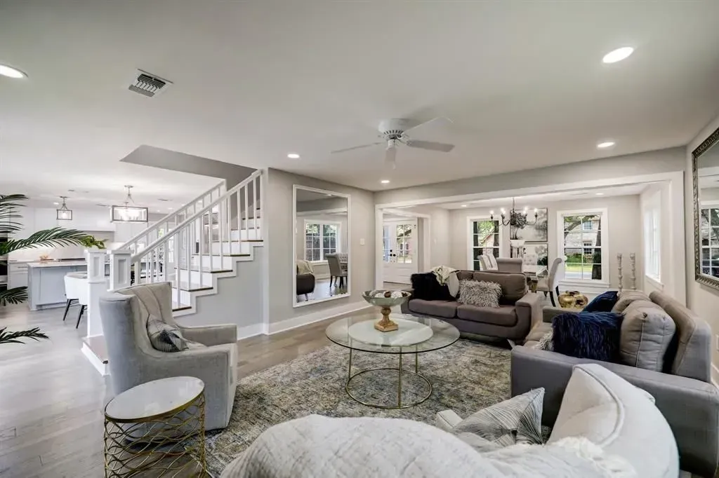 Bright modern living room with white staircase, gray sofas, round coffee table, and large windows