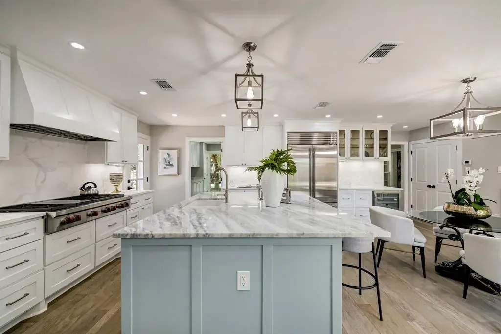 Bright modern kitchen with marble island, white cabinets, and dining area in the background