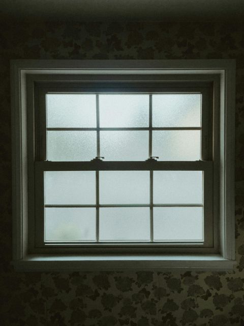 Dim window with six frosted panes above patterned wallpaper indoors