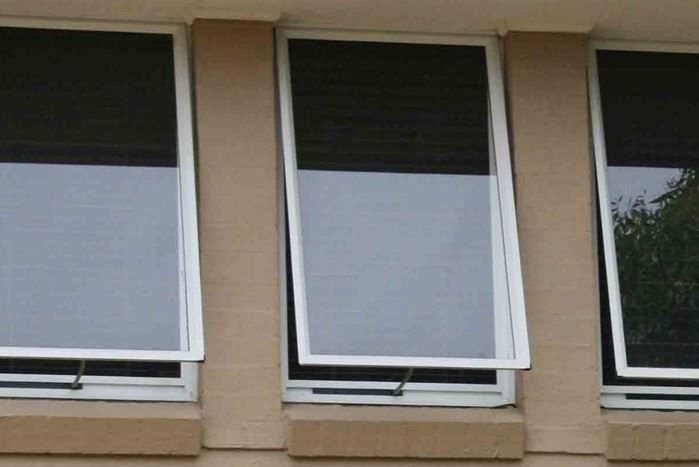Three windows on a beige building, with dark upper panes and white blinds partly lowered