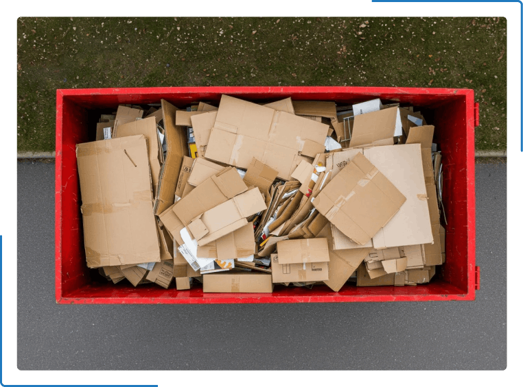 A red dumpster filled with cardboard boxes is sitting on the side of the road.