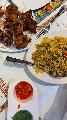 Fried snacks, rice dish, and dipping sauces on plates at a restaurant.