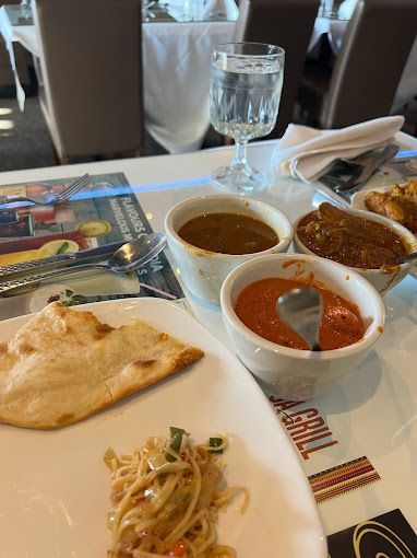 Indian food spread on a white table: naan, noodles, sauces, and a glass of water.