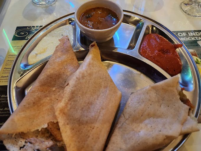 Three dosa crepes on a divided metal plate with sauces, served at an Indian restaurant.