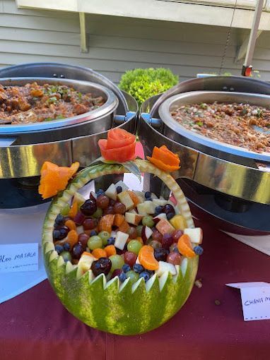 Fruit salad in a carved watermelon basket with two chafing dishes in the background.