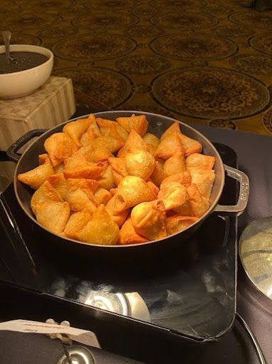 Bowl of golden-brown samosas on a buffet with a small bowl of dark dipping sauce.