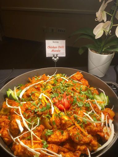 Chicken chili masala in a serving dish, garnished with greens and vegetables.