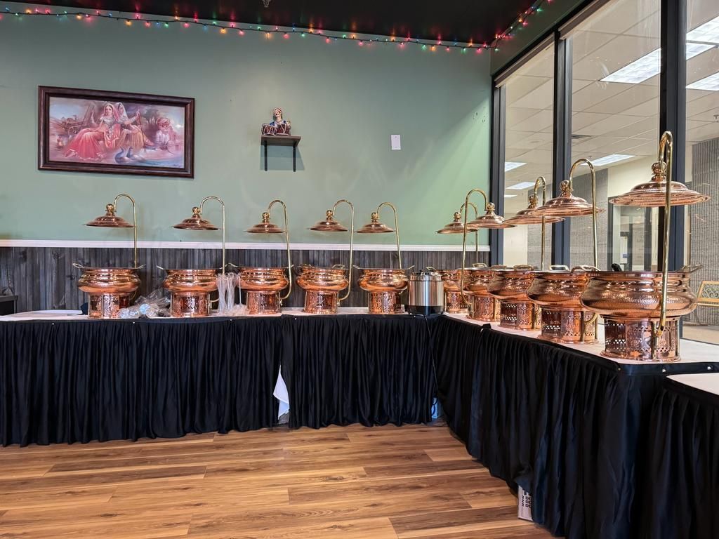 Buffet setup with copper serving dishes, black table skirt, and overhead lamps in a restaurant.