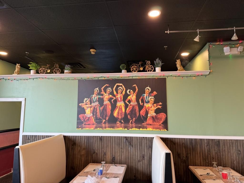 Interior of an Indian restaurant with a dance scene mural above booths.