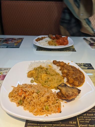 Plates of Indian food on a white table: rice, curry, fried rice, and chicken.