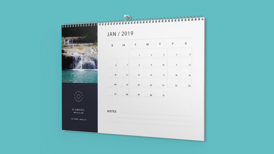 A calendar with a picture of a waterfall on it is hanging on a blue wall.