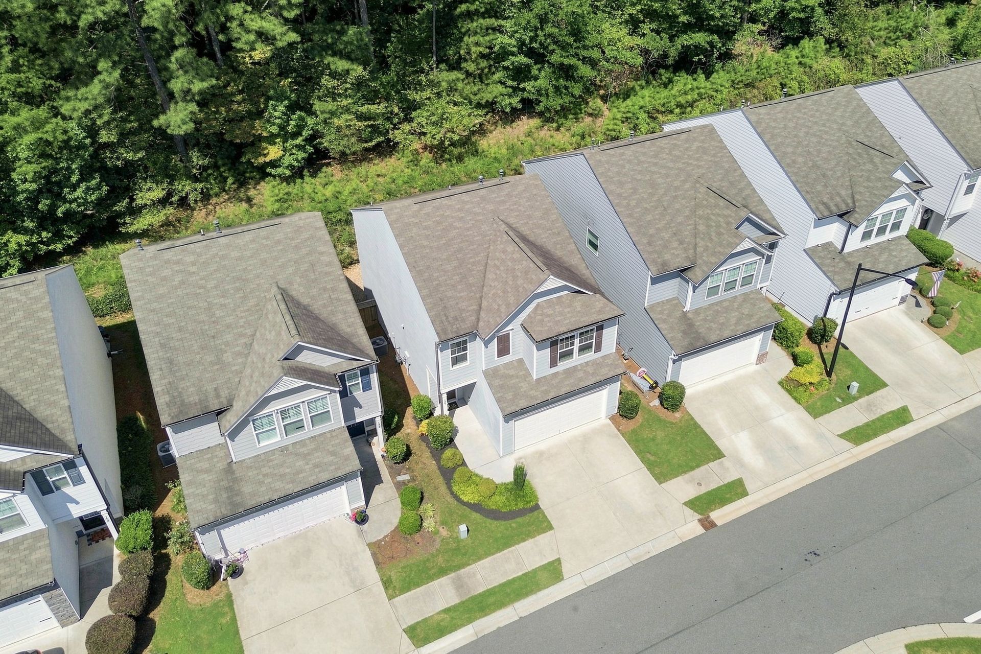Aerial view of suburban homes with driveways and green lawns beside a tree-lined street
