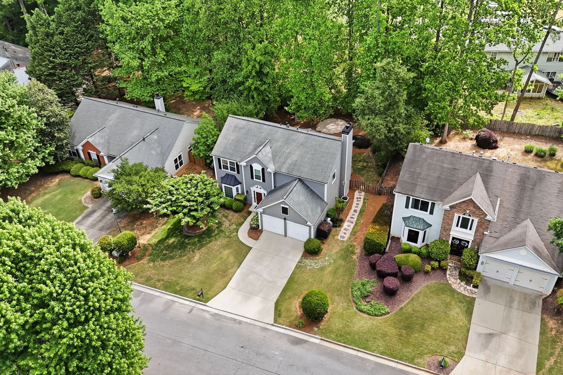 Aerial view of three suburban houses with driveways, lawns, and trees along a curved street.