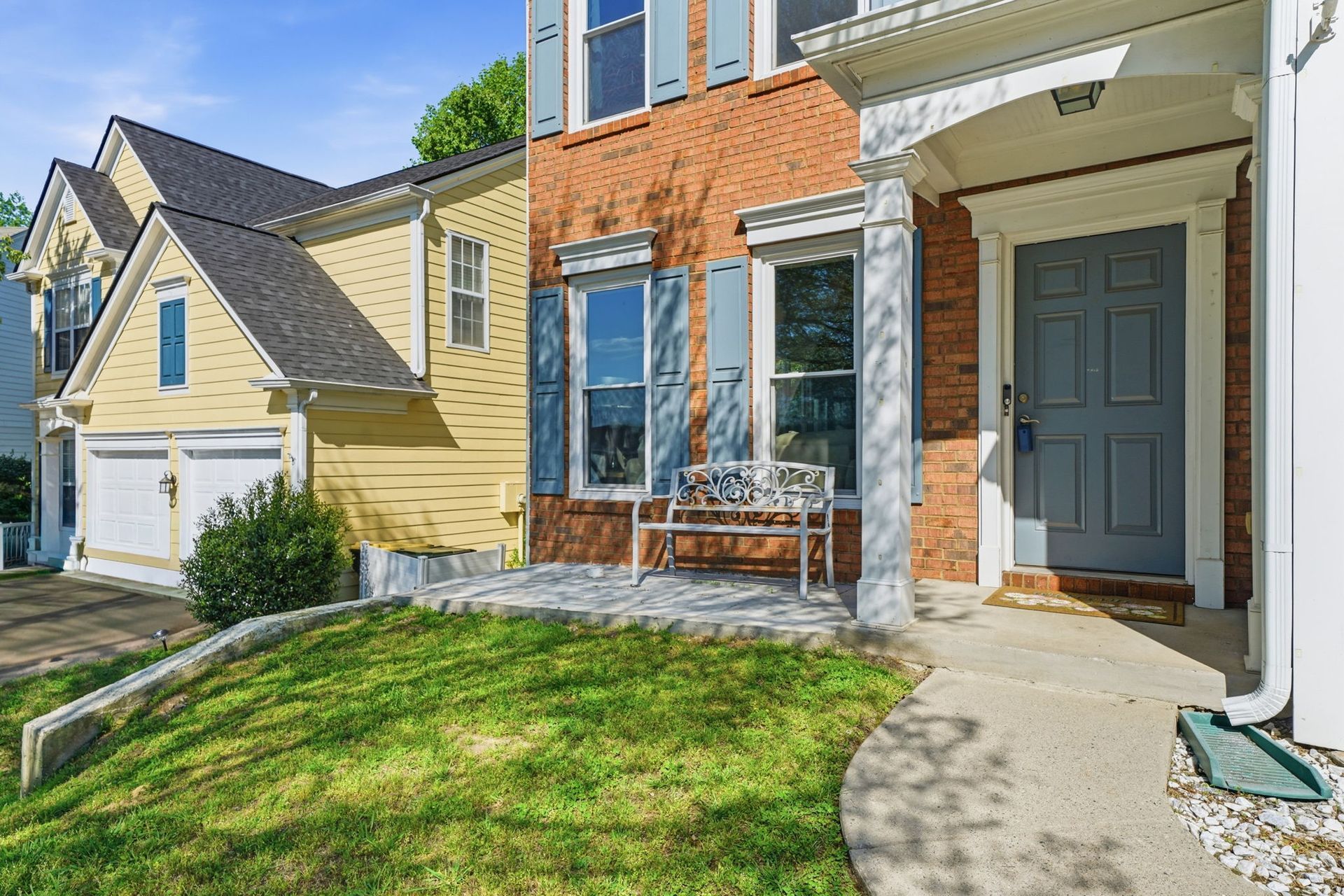 Brick townhouse entrance with blue door, white trim, and a small grassy front lawn