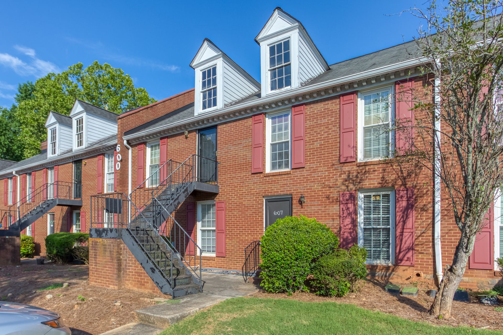 Brick apartment building with white dormers, red shutters, and exterior staircases under a blue sky