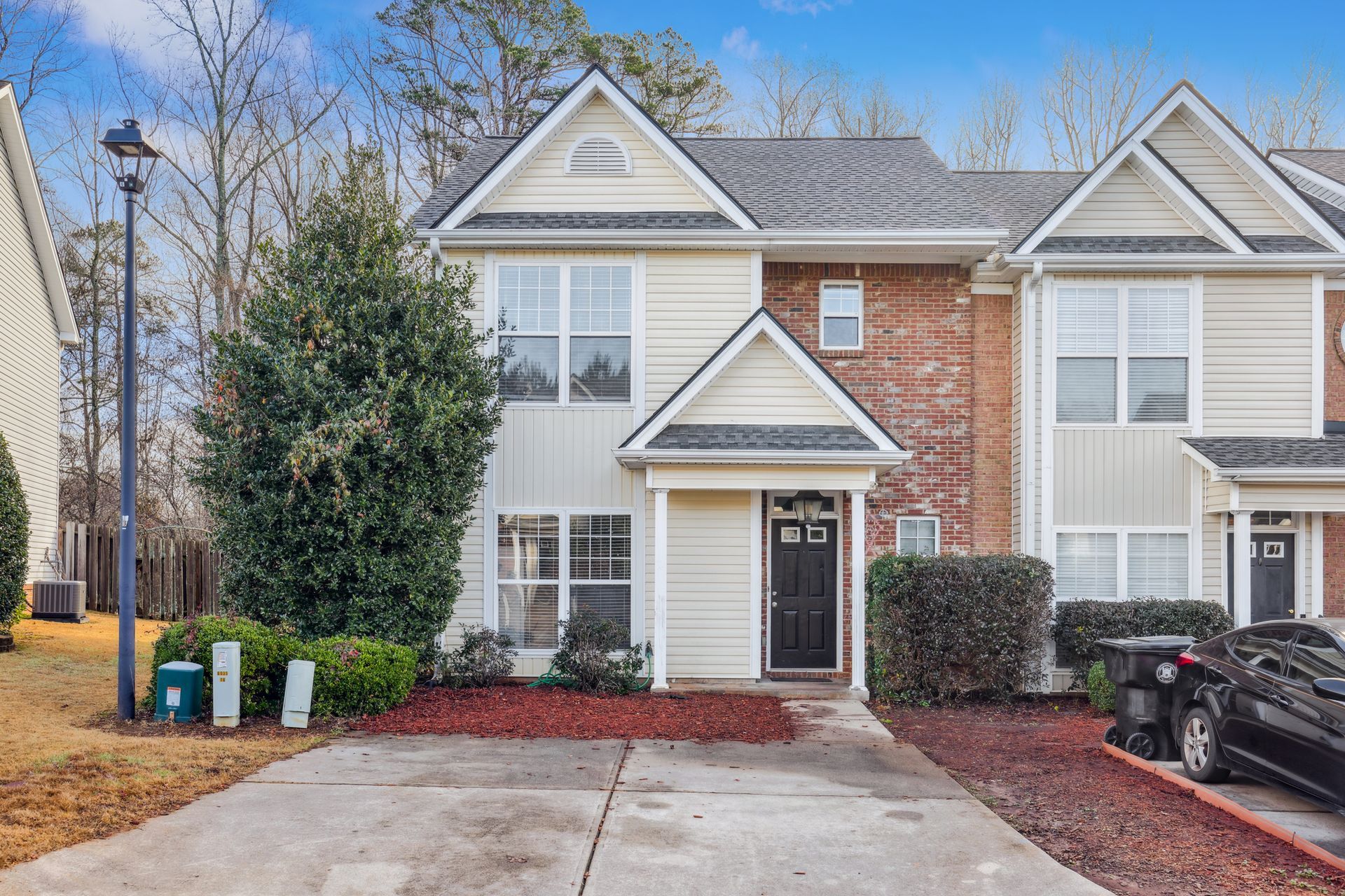 Two-story beige townhouse with black door, brick accents, and driveway.