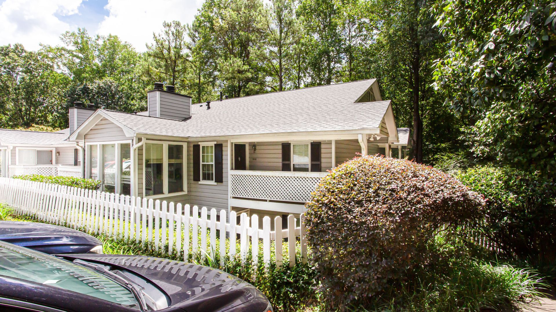 Cottage-style home with white picket fence, gray siding, and lush green trees in the background.