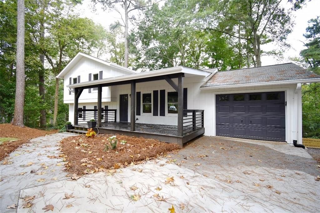 White house with black trim and garage, set among trees with a curved driveway and fallen leaves.