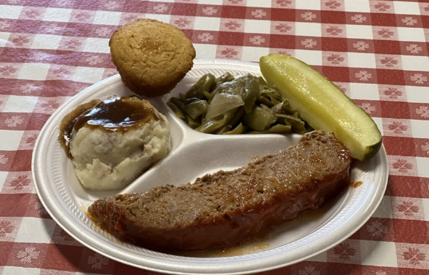 Plate of food: meatloaf, mashed potatoes with gravy, green beans, pickle, and cornbread muffin.