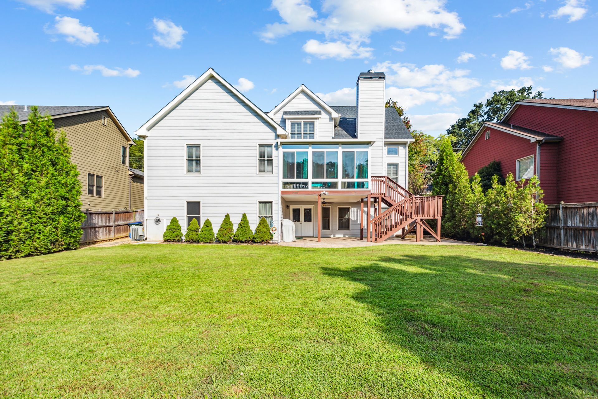 White two-story house with a glass deck and wooden stairs, viewed from a large green backyard