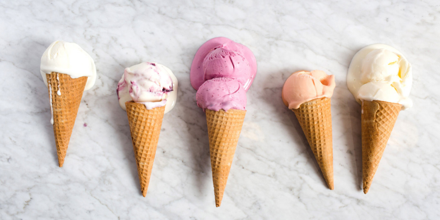 Five ice cream cones with different colored scoops on a marble surface.