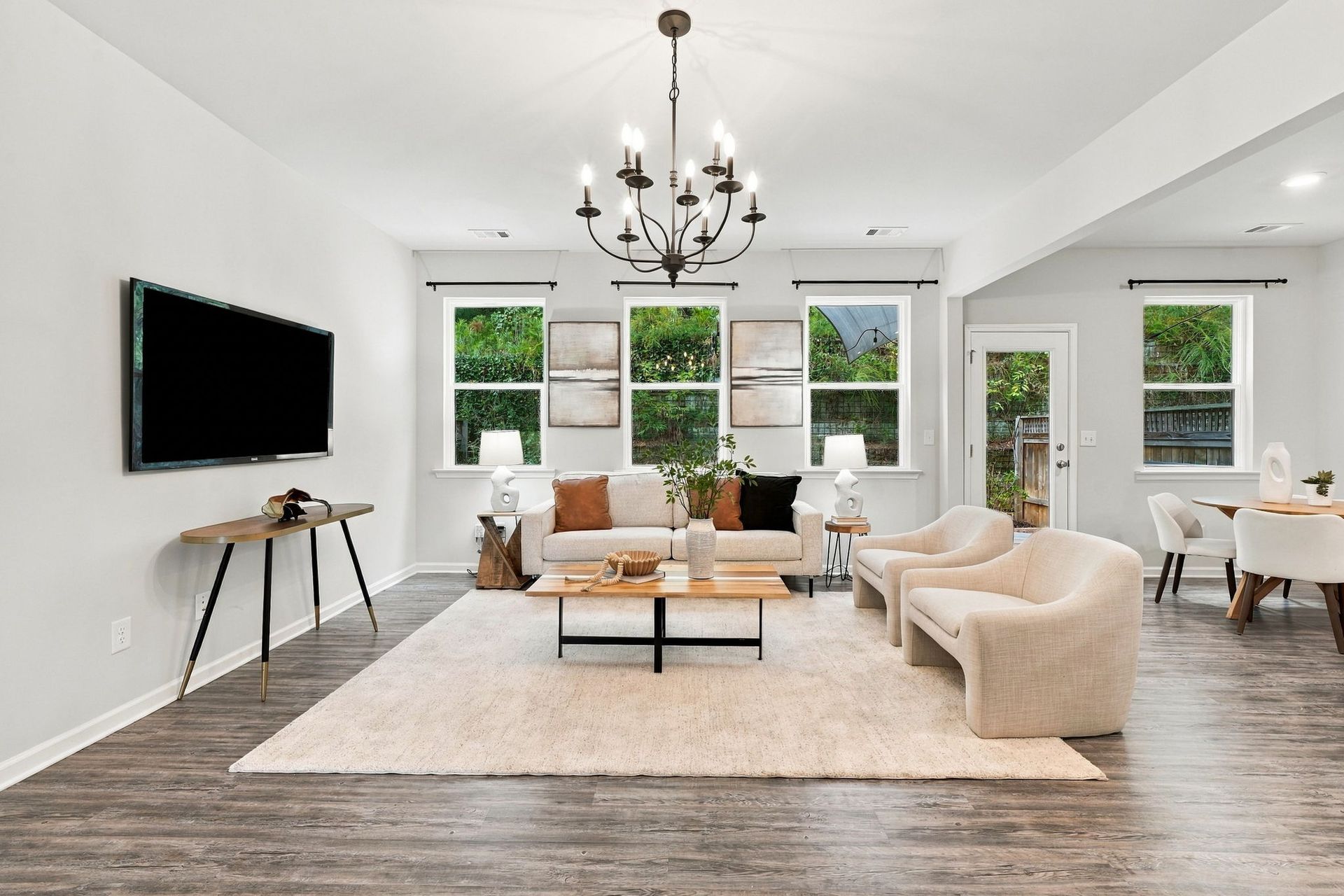 Bright modern living room with cream sofas, chandelier, wall-mounted TV, and large windows.