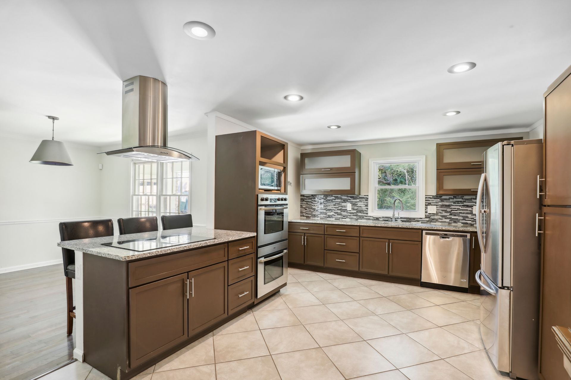 Modern kitchen with brown cabinets, stainless steel appliances, marble island, and tiled floor