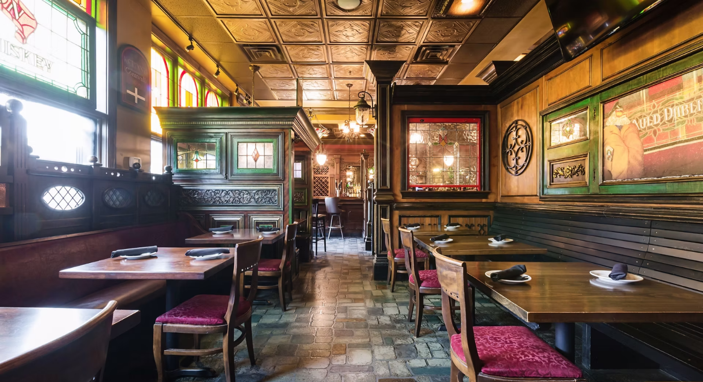 Interior of a dark wood-paneled pub with tables, chairs, and stained glass windows.