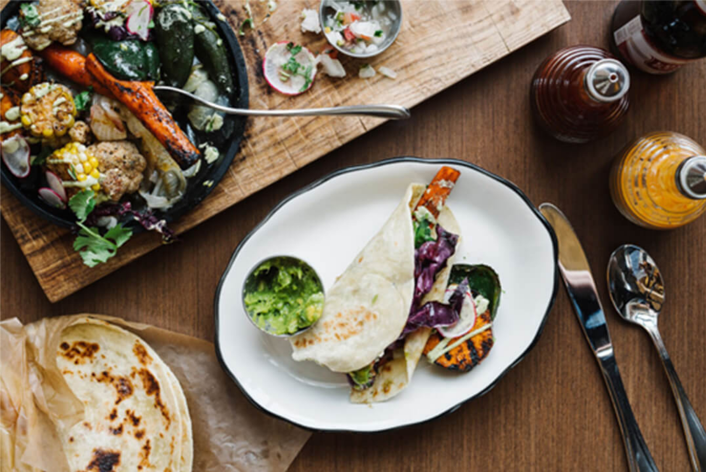 Grilled vegetables and a taco on a plate with salsa and sauces on a wooden table.