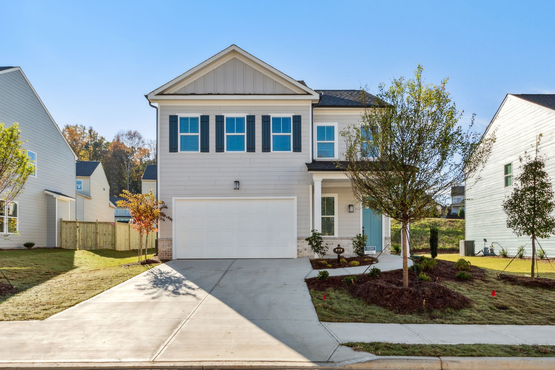 Two-story suburban house with white garage, blue shutters, driveway, and landscaped front yard