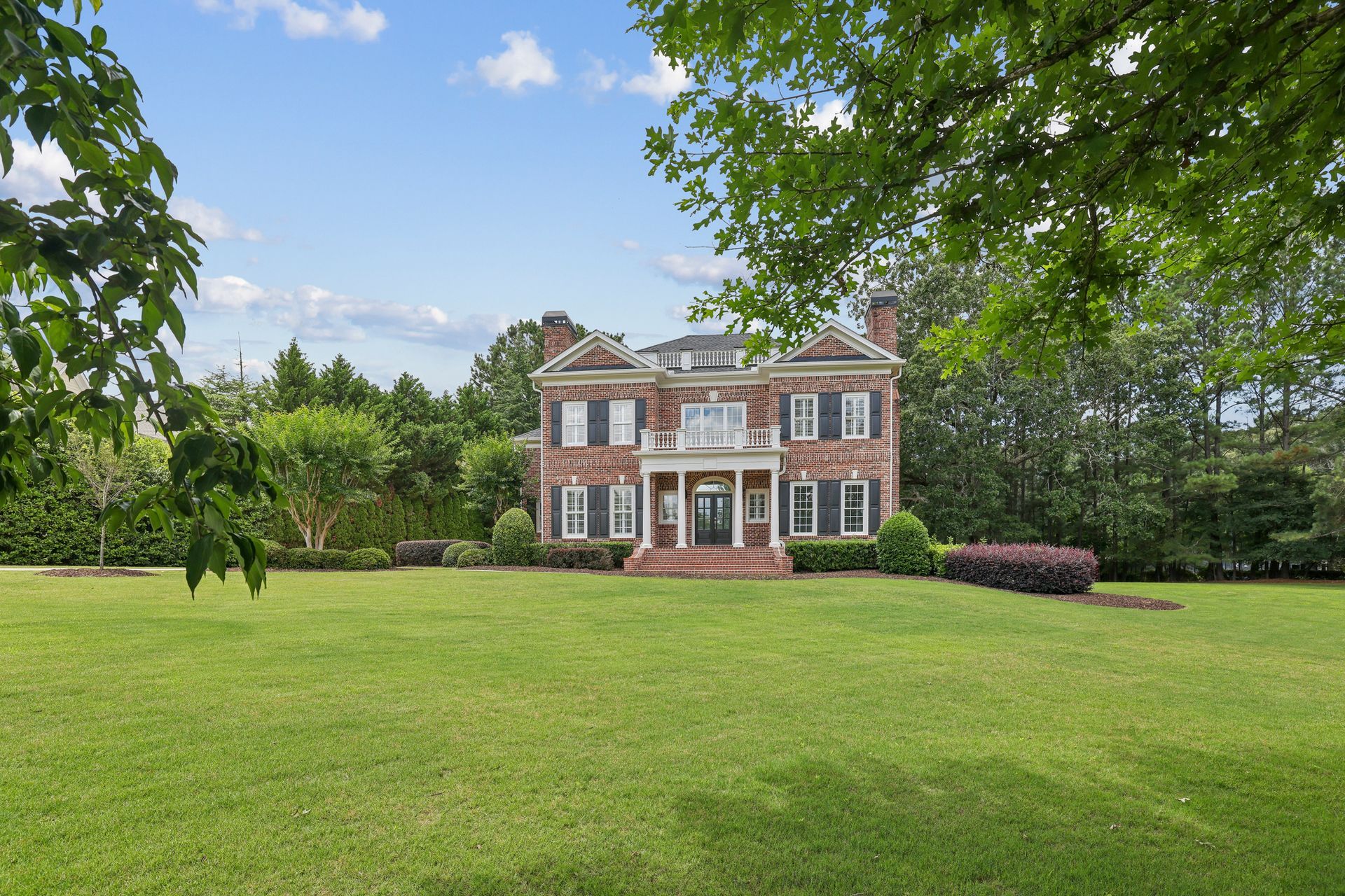 Large brick house with white trim on a spacious green lawn, framed by trees under a blue sky