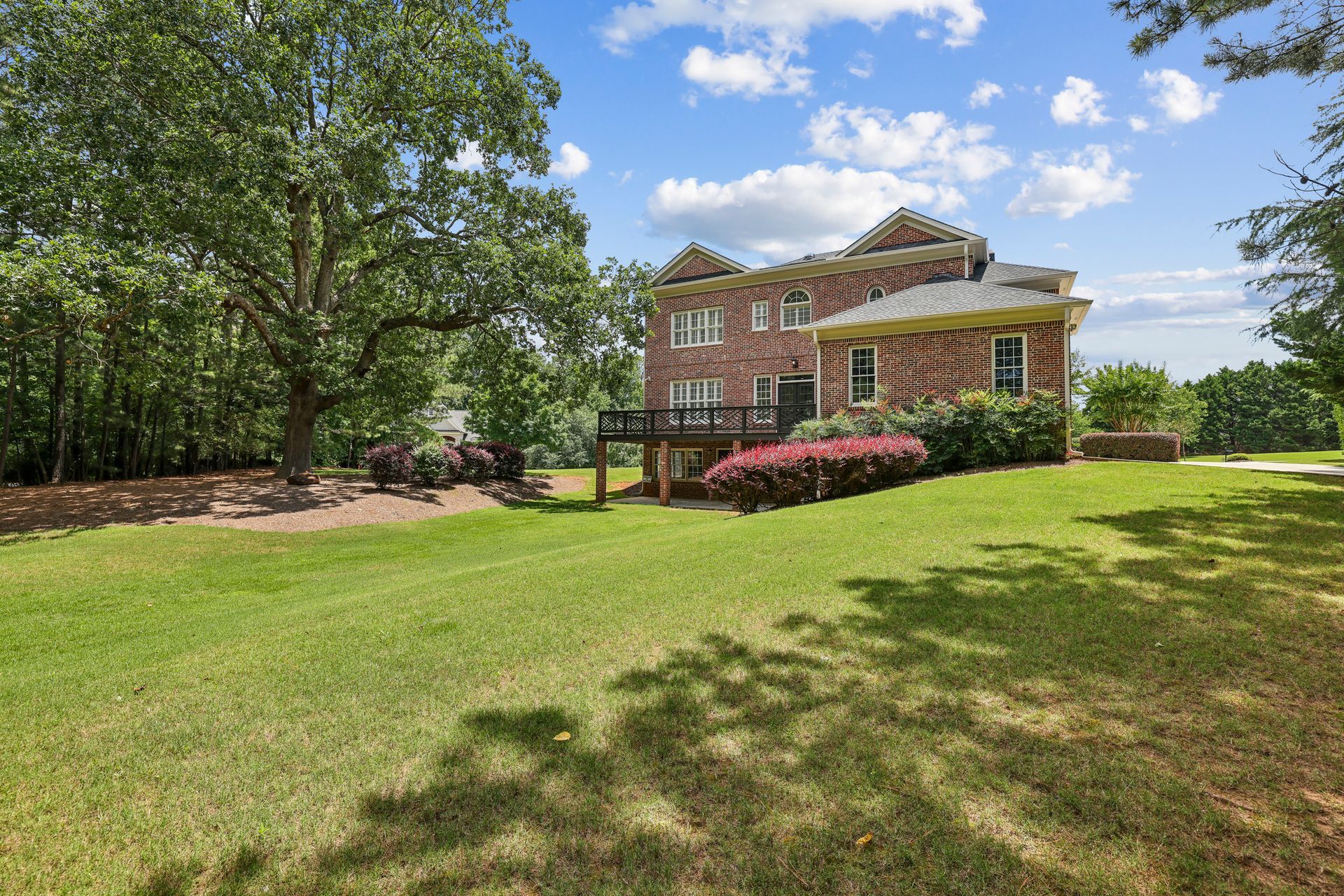 Brick house with a covered porch, surrounded by a large green lawn and trees under a blue sky