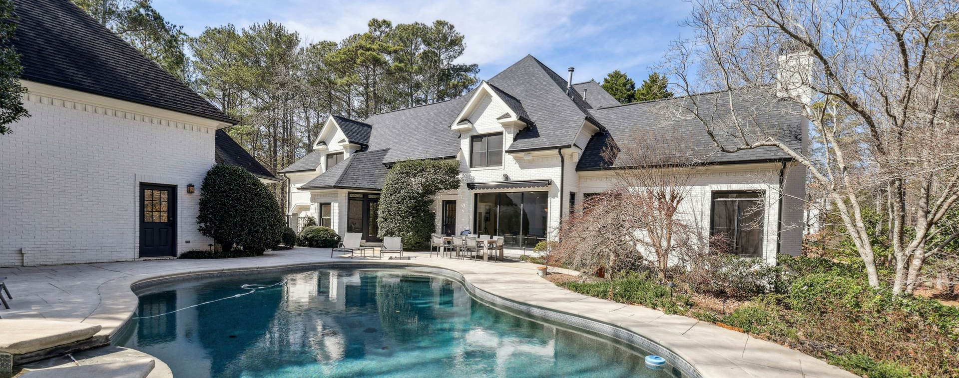 Backyard pool beside a large white house with a patio and trees