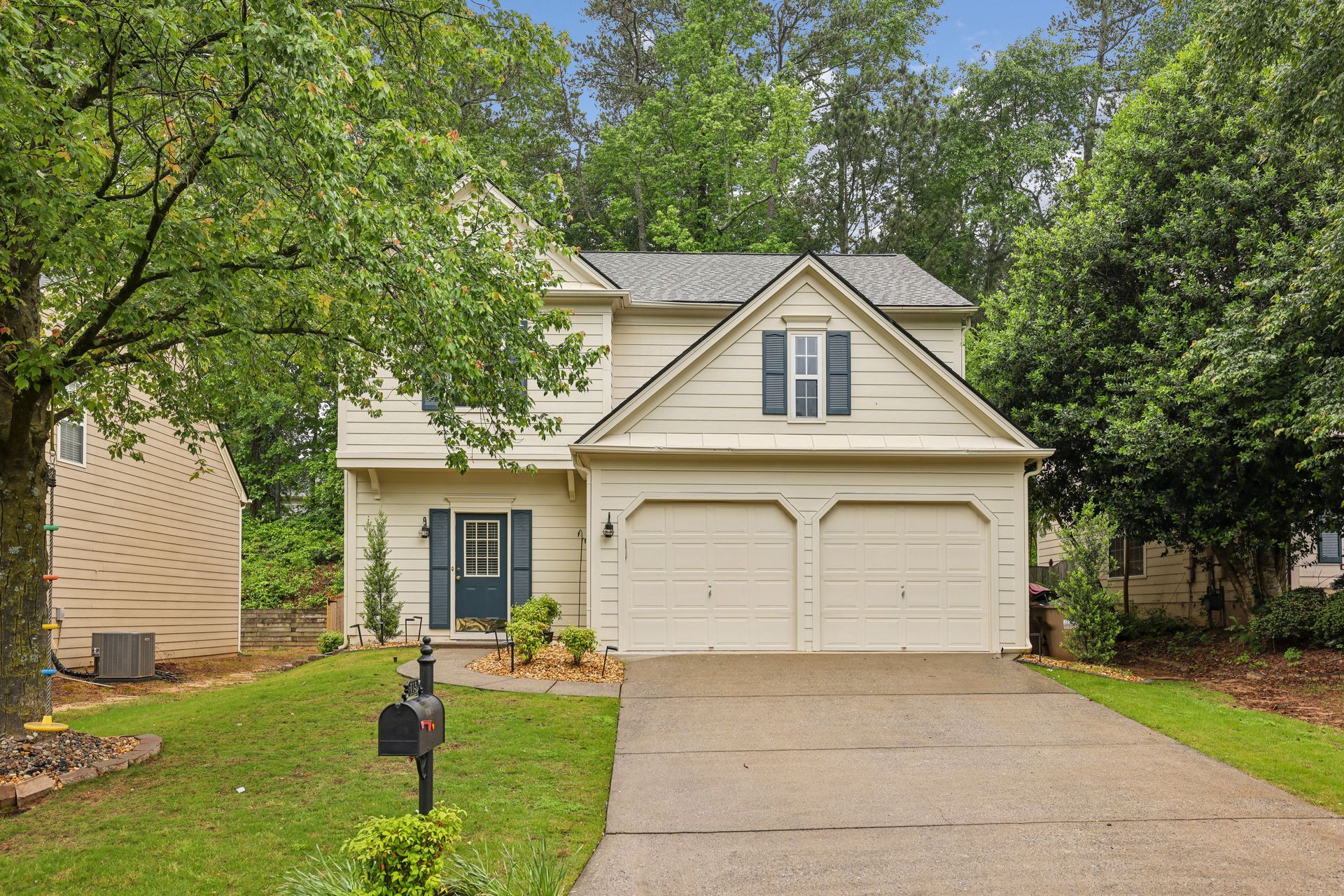 Beige two-story house with a two-car garage, blue shutters, and a mailbox on a green lawn.