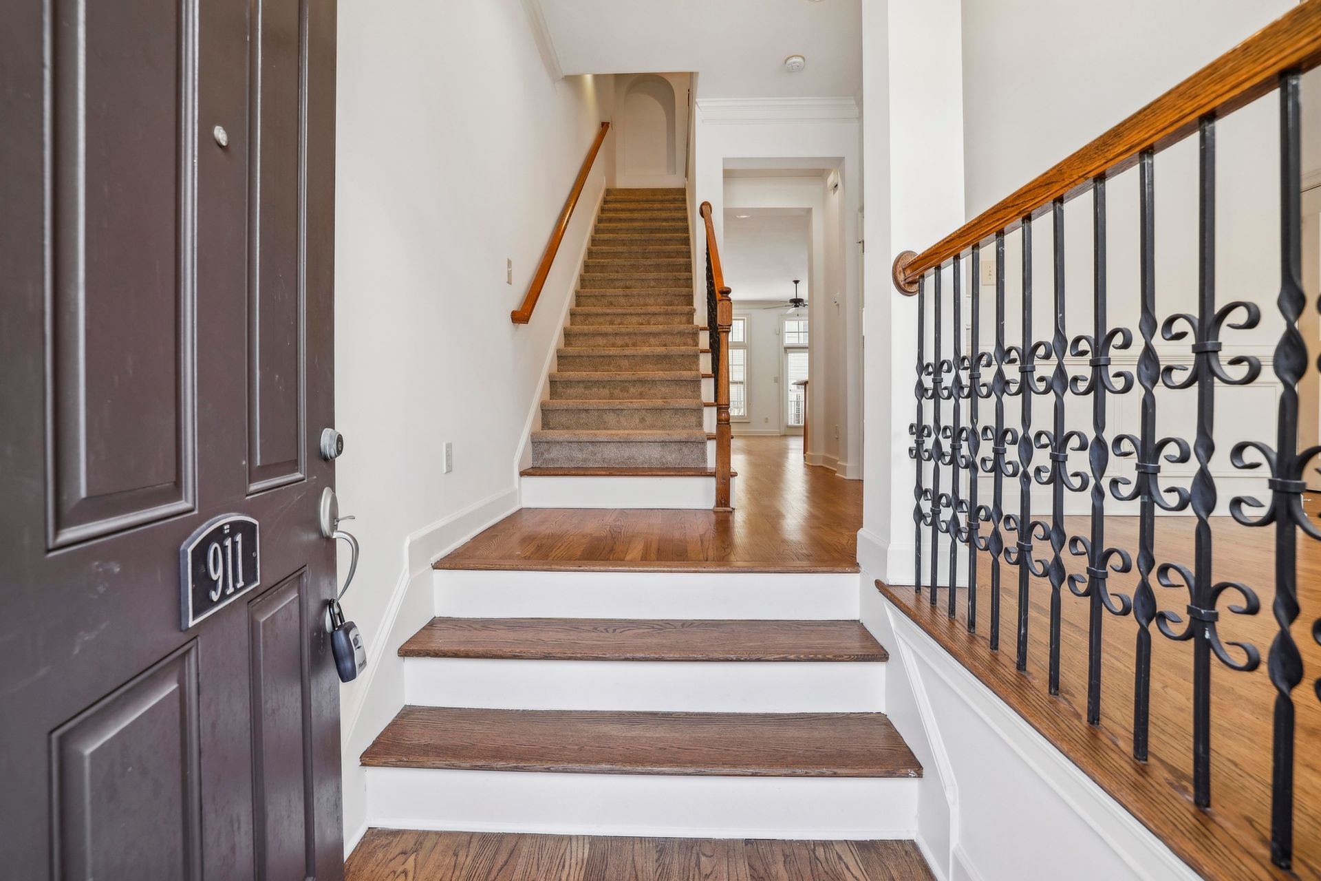 Interior entryway with carpeted stairs, white walls, and a dark front door with wrought-iron railing