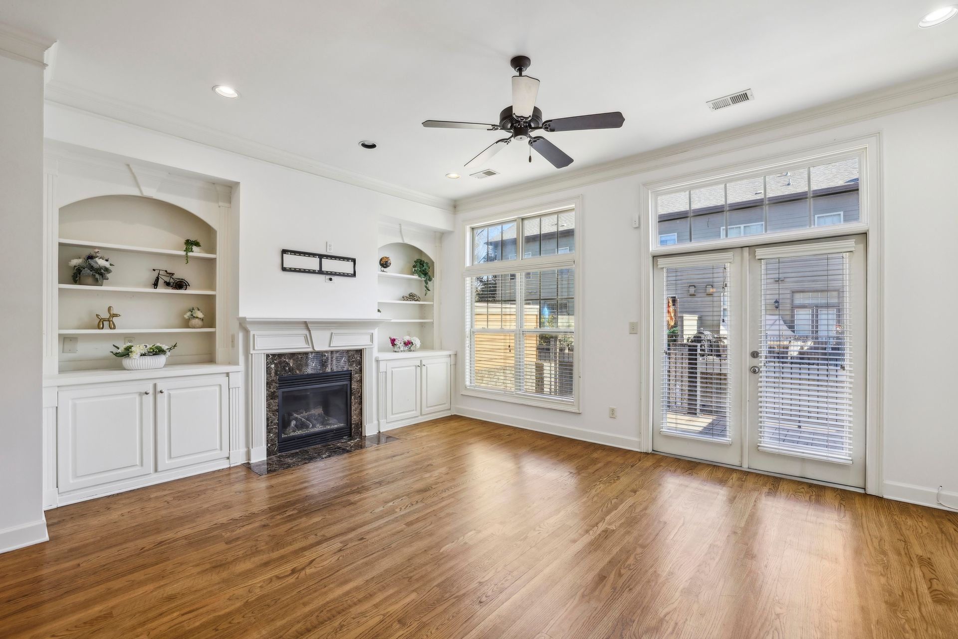 Bright living room with hardwood floors, white walls, fireplace, and large windows with a glass door.