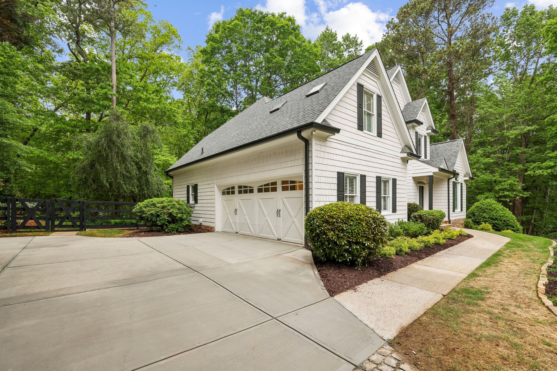 White two-story house with attached garage, driveway, and trees in a wooded yard