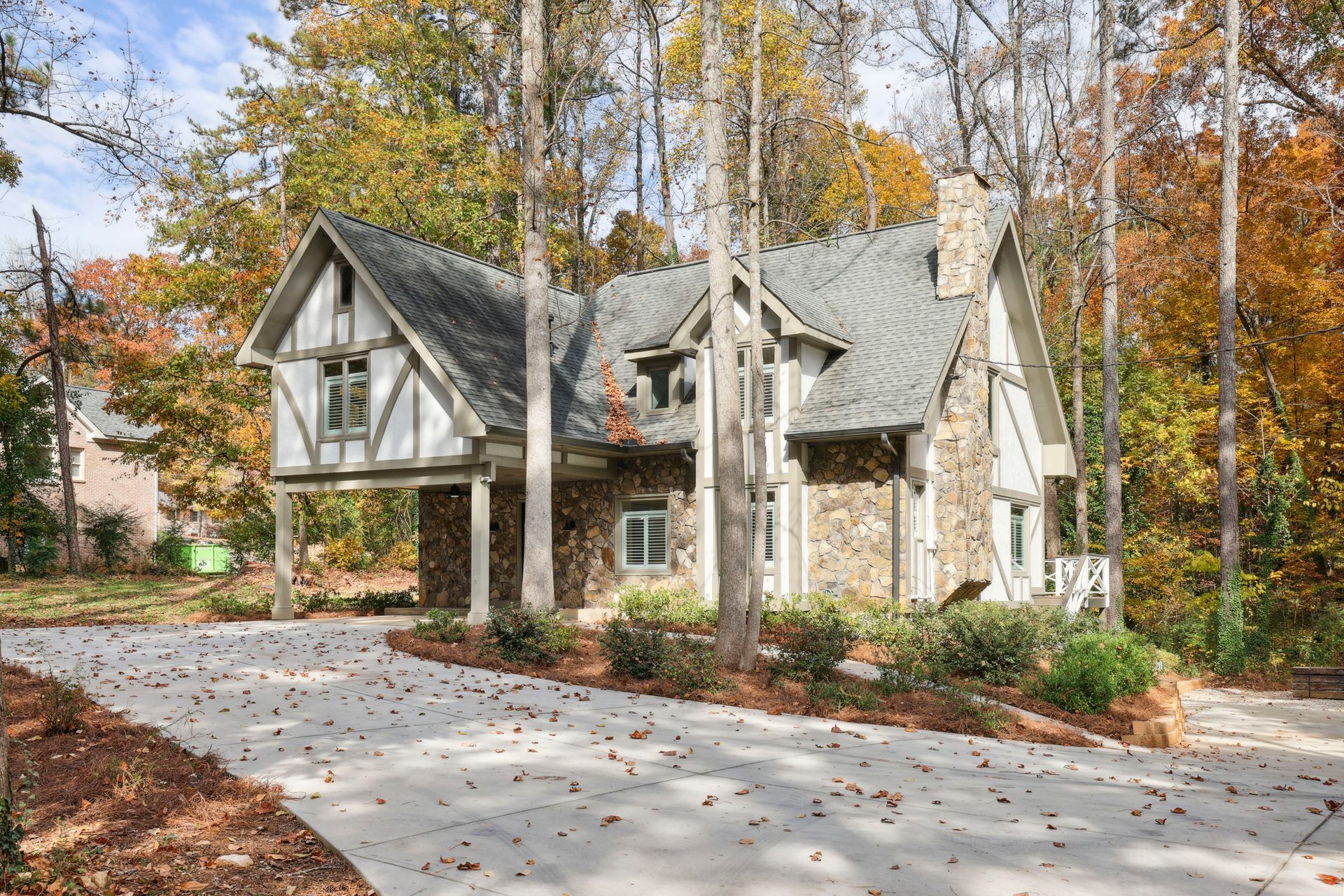 Stone Tudor-style house with steep gray roof amid autumn trees beside a curved driveway