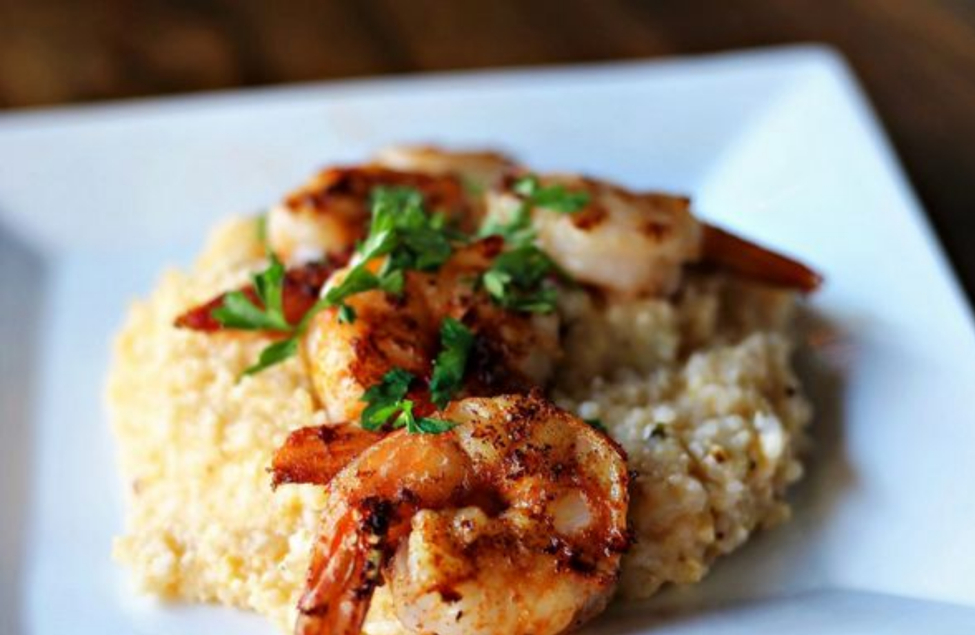 Shrimp and grits dish on a white plate, topped with parsley.