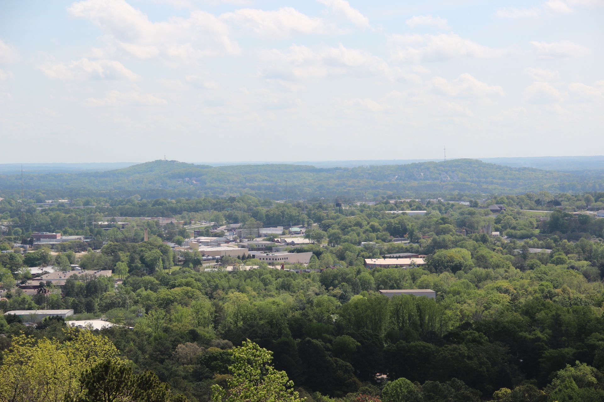 Overhead view of a town surrounded by green trees under a hazy sky.