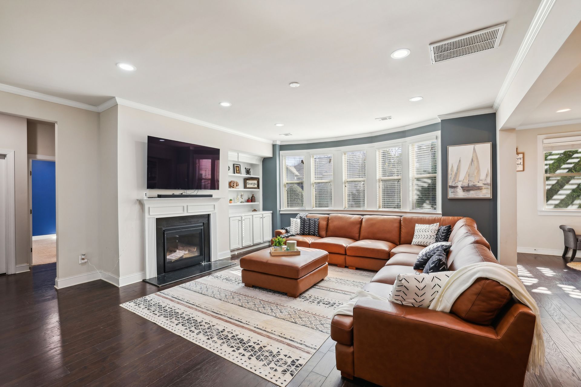 Living room with brown leather sectional, fireplace, TV, and large bay window.