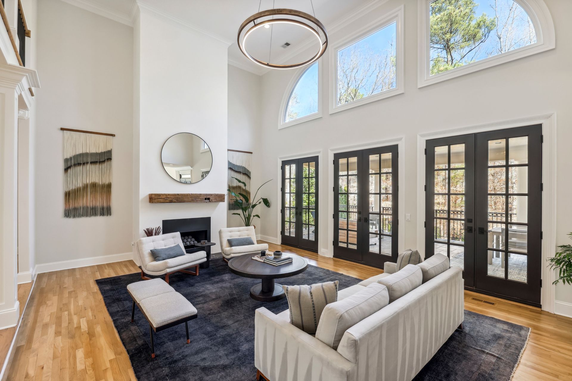Spacious living room with high ceilings, large windows, and dark blue rug; neutral-toned furniture.